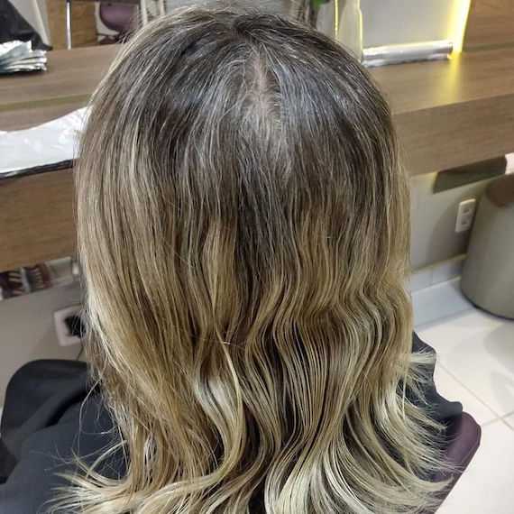 The back of the head of a woman with wavy blond hair and gray lines.